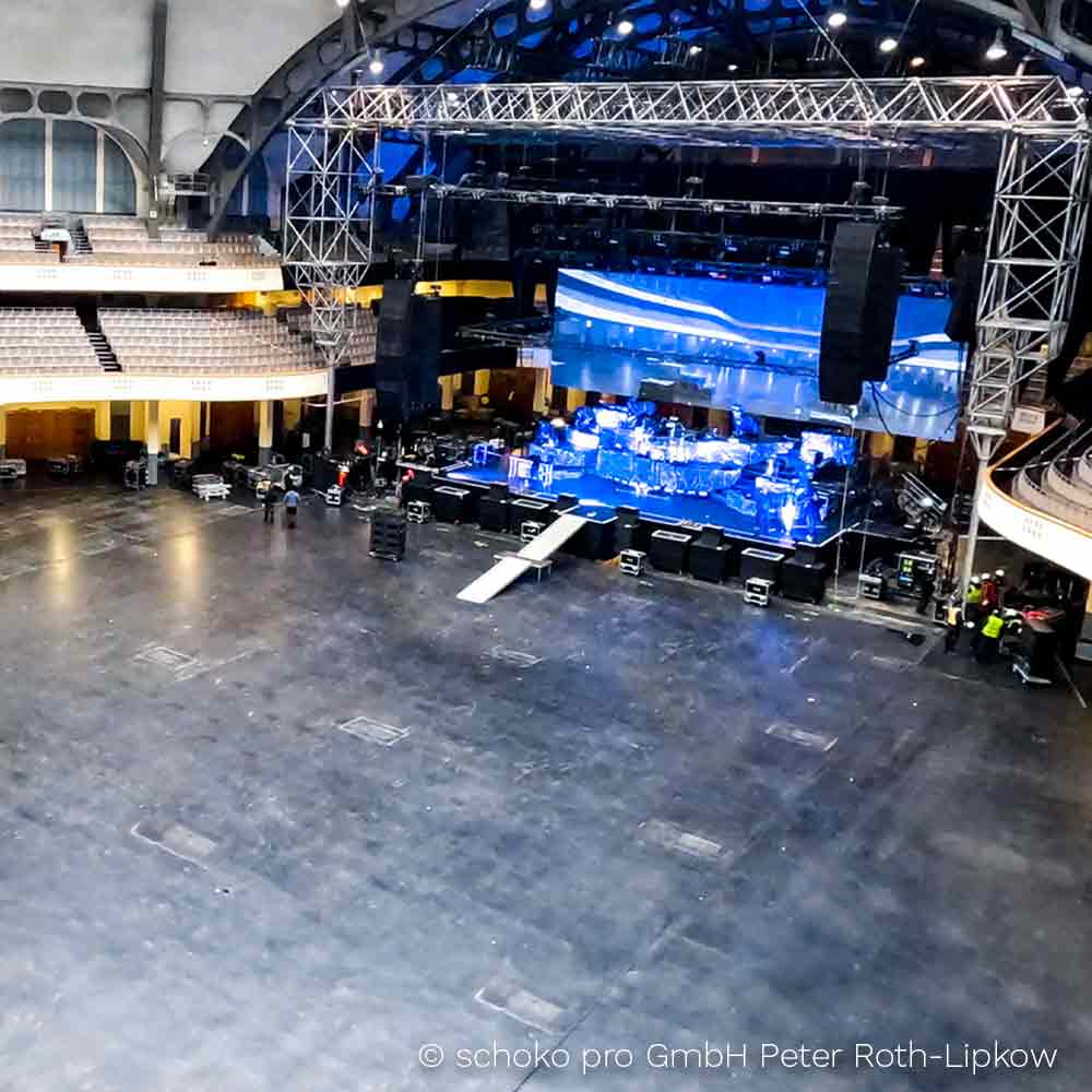 Grosse leere Konzerthalle mit moderner Bühne, blau beleuchtetem Hintergrund und Technikpersonal