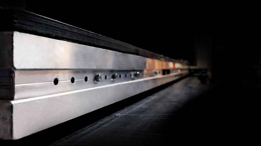 Eine glänzende Metallschiene mit Bohrungen liegt in einem dunklen Umfeld